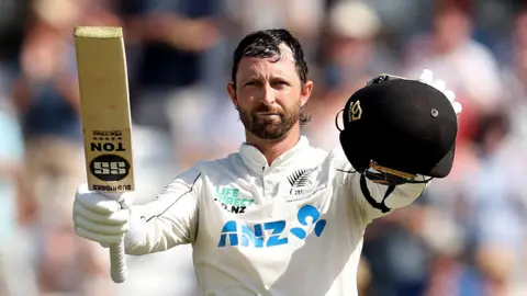 New Zealand batter Devon Conway raises his bat and helmet after hitting a century