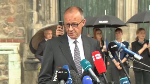 German chancellor in a suit speaking into microphones.