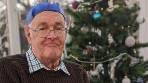 Michael Wilson sat in front of a Christmas tree whilst wearing a Christmas party hat and glasses