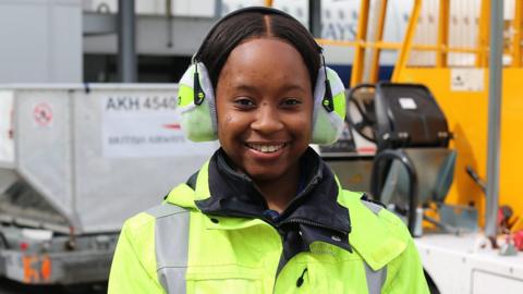 A woman on a construction site wearing high visibility clothing and ear protectors.