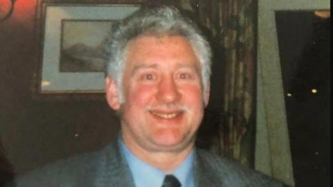 James Joseph Corrigan wearing a suit and tie with grey hair and moustache 