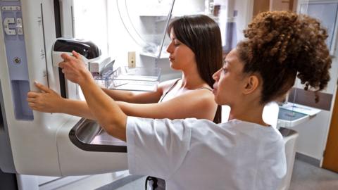 A radiographer provides assistance to a patient undergoing a mammogram in a modern medical facility
