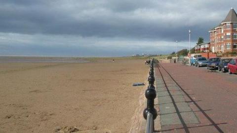 Beach on one side of path and cars on other side - a metal fence is in the middle 