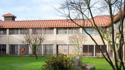 Part of HMP Bullingdon, showing a lawn with small trees, enclosed by a two-storey building with glass doors and windows.