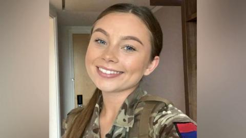 Gunner Jaysley Beck smiles in a selfie wearing a khaki camouflage jacket.