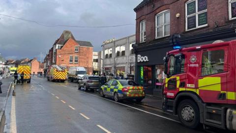 Baxter Street in Loughborough with emergency vehicles parked at the side of the road, either side of police tape which is stretched across the highway.
