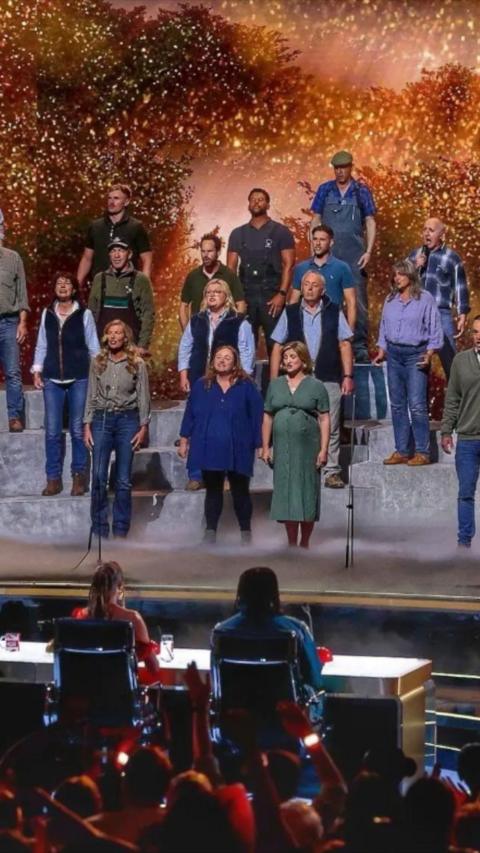 The Hawkstone Farmers Choir performs on the Britain’s Got Talent stage in front of the judges and a packed audience. Bathed in golden lights and sparkling effects, the choir delivers a powerful performance that celebrates rural life and community spirit. Standing on tiered platforms, the singers are led by their conductor as they captivate the crowd with an emotional and uplifting rendition.