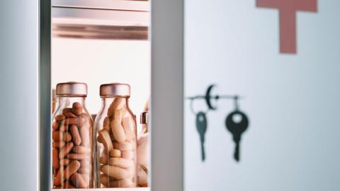 An open medicine cabinet door, with a key in the locks, reveals bottles of pills inside