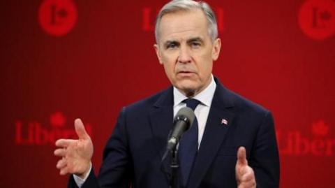 Mark Carney in a dark suit gesturing with hands against a red backdrop of Liberal Party