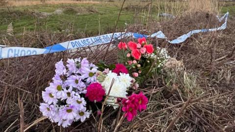 Flowers on some grass under some police tape 