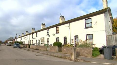 A row of white terraced houses with some cars parked outside.