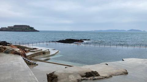 Bathing pools in Guernsey. The ocean and rocks are in the background. Steps lead down into the bathing pool.
