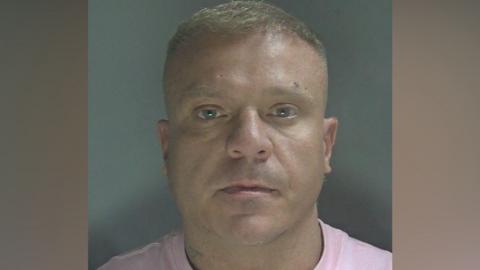 Custody photo of a man with short light hair and a pink t-shirt