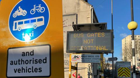 Picture of a sign allowing only buses, scooters and taxis through to a street in Barton Hill, in Bristol, where a bus gate has been put in during the night. In the background is a sign which reads "bus gate not operational".