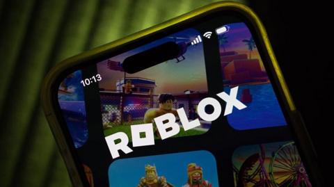 The Roblox logo on a phone with a dark backdrop and silhouette.