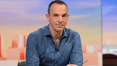 Martin Lewis sat in a TV studio wearing a light blue shirt.