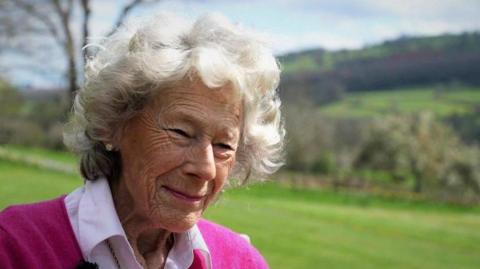 Dame Shân, with short grey hair and wearing a pink jumper and shirt.