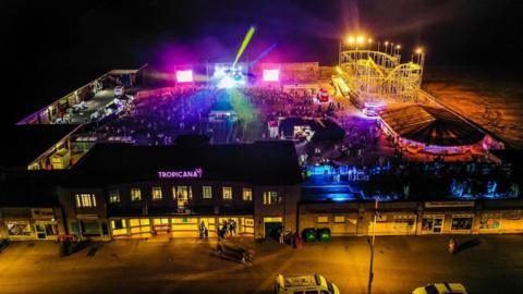 A drone shot of The Tropicana at night with a stage, lights, and a crowd watching a performance.