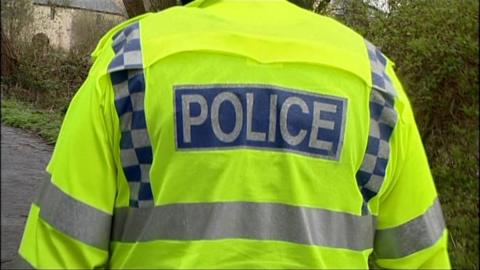 Close up of the back of a police man in high visibility fluorescent jacket with the word POLICE visible