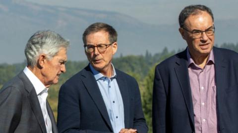 Jerome Powell, chairman of the US Federal Reserve, Tiff Macklem, governor of the Bank of Canada and Andrew Bailey, governor of the Bank of England stand in front of a scenic mountain view. There are all wearing dark-coloured blazers with shirts.