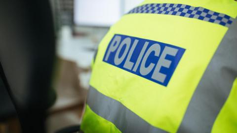 A police officer's back. It shows the word 'police' in capital letters and the jacket the officer is wearing is yellow. 