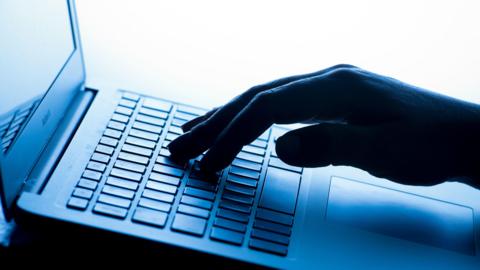 A silhouette image of a hand pressing buttons on a laptop keyboard.