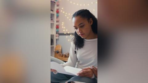 A teenager looks at a sheet of paper in her bedroom.