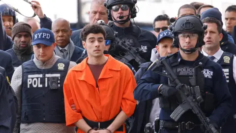 Luigi Mangione, the suspect in the murder of UnitedHealth Group executive Brian Thompson, arrives at a helicopter pad after being extradited from Pennsylvania, as Mayor Eric Adams walks behind him, in New York