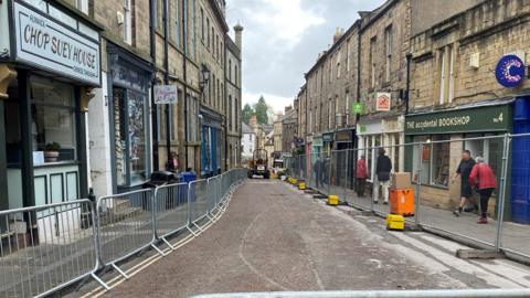 A narrow 18th Century road with railings on either side and in the distance there is a digger. 