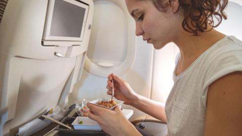 A woman eating from a carton on a plane