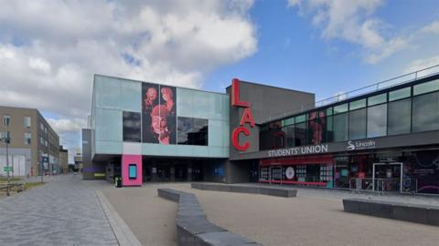 Exterior of the Lincoln Arts Centre it is a glass and concrete two-storey building with the letters LAC in red on one wall