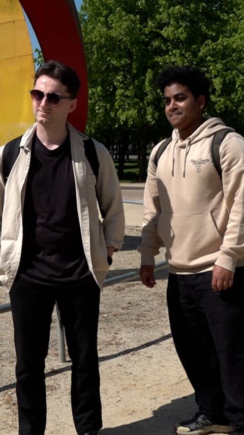 Two men standing in a park on a very sunny day.