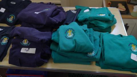 A table with school uniform on it. The uniforms are navy blue and turquoise and have a school badge on it.