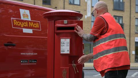 A postman is seen opening a post box 