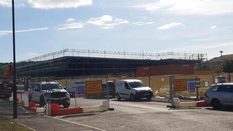 The new Aldi supermarket is under construction. The large warehouse is surrounded by scaffolding and fencing.