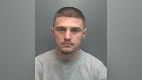 A police mugshot of a man with short hair and a light beard.