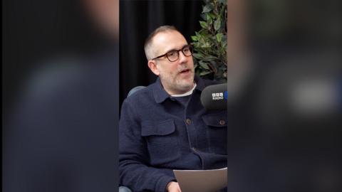 Dr Xand speaks into a microphone while holding a letter