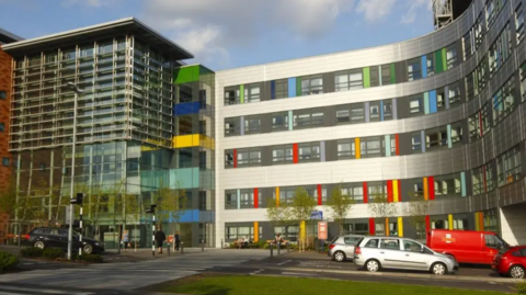 Outside of the Queen Alexandra Hospital building which is made of glass and has colourful tiles at the front.