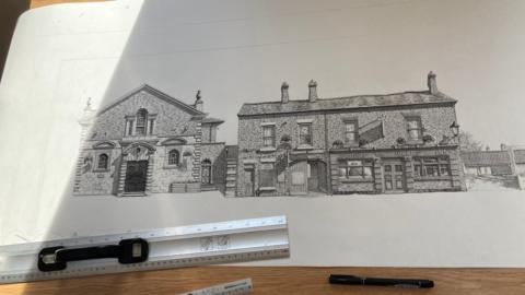 A line drawing of buildings in a historic street, with a medieval guildhall on the left and shops on the right