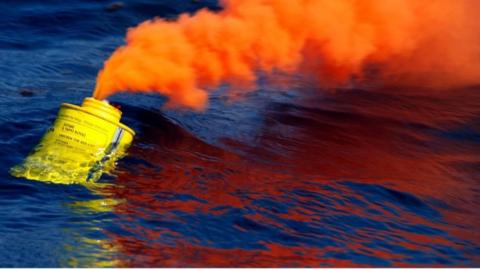 A flare floats in the ocean giving off orange smoke.
