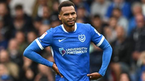 Portsmouth winger Josh Murphy puts his hands on his hips and looks bemused. he wears an all blue portsmouth fc top with long sleeves