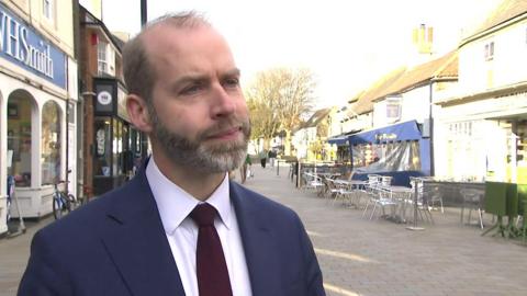 A man in a suit on a sunny high street. 