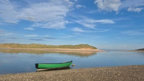 A sunny beach scene at Newburgh in Aberdeenshire, with a green rowing boat in the water.