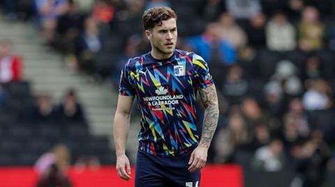 Charlie McCann standing on the pitch during a game for Barrow with his arms by his side