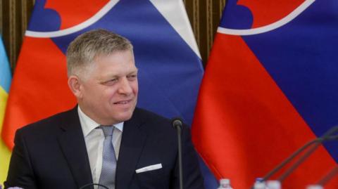 Robert Fico smiling with Slovak flags in background