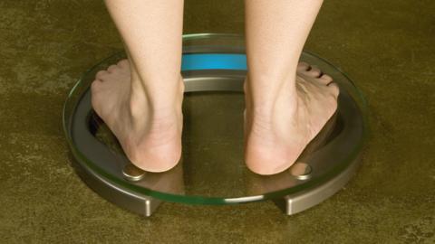 A person standing barefoot on a round set of scales made of glass.