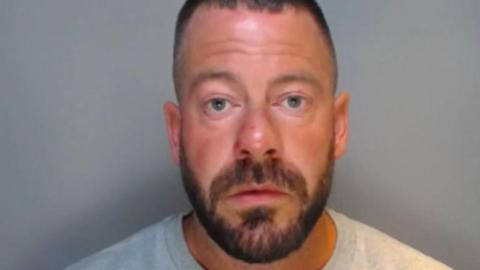 Mugshot of a man with a short dark beard and hair