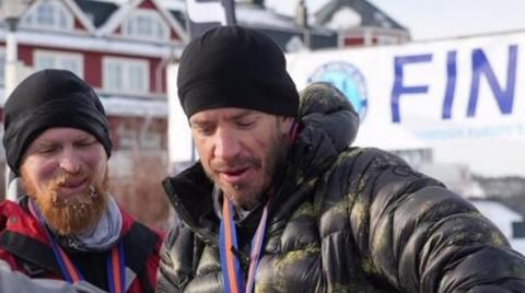 Karl Hinett, with a beard, on the left of the photo, is with another man, who is also wearing a black hat, at the finish.