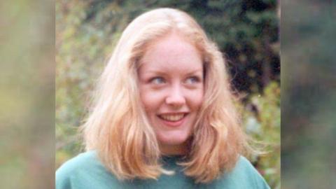 A family photo of Fleur Lombard. She has blonde shoulder-length hair and is looking away from the camera smiling in what appears to be a garden or park. 