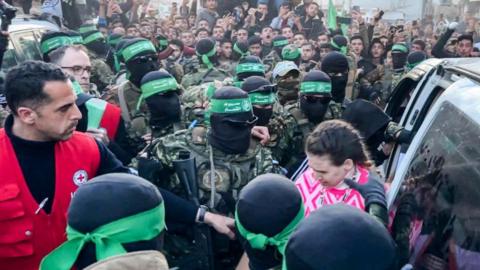 One of the three Israeli hostages released on Sunday in Gaza is handed over by Hamas fighters to a member of the Red Cross.